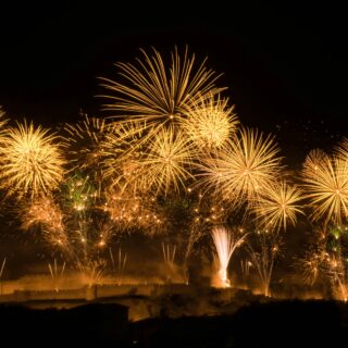 Golden fireworks erupt across a dark night sky over a silhouetted cityscape.