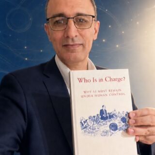 Man in a suit and glasses holding a white book titled 'Who Is in Charge?' about AI and human control.