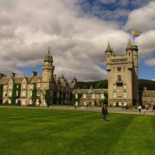 Castle with turrets and a yellow flag, set against a cloudy sky and green lawn.
