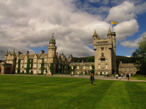 Castle with turrets and a yellow flag, set against a cloudy sky and green lawn.