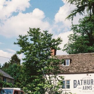 Front of a white brick pub with a large Bathurst Arms sign, framed by green trees against a blue sky with clouds.