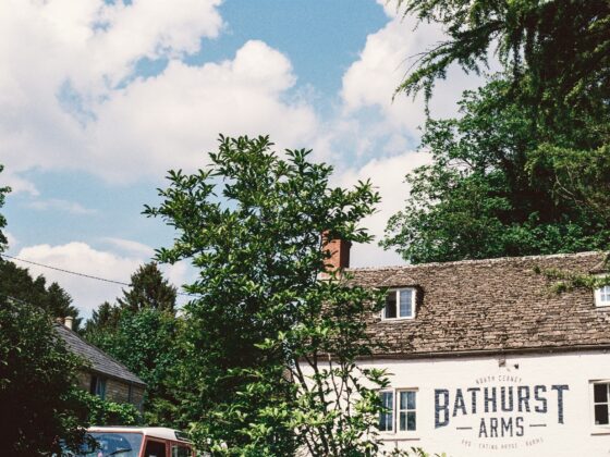 Front of a white brick pub with a large Bathurst Arms sign, framed by green trees against a blue sky with clouds.
