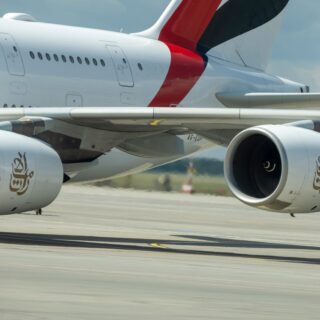 Large commercial airliner on the tarmac, showing two engines and a white fuselage with a red and dark tail design.
