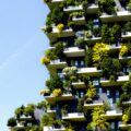 High-rise residential building with many balconies covered in plants against a clear blue sky.