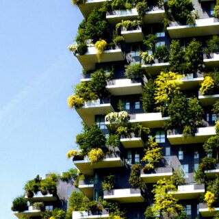 High-rise residential building with many balconies covered in plants against a clear blue sky.