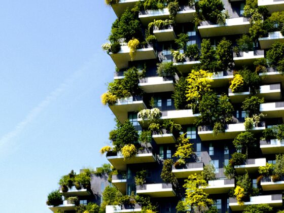 High-rise residential building with many balconies covered in plants against a clear blue sky.