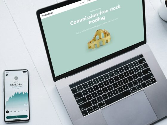 Laptop screen shows Wealthsimple Trade promo for commission-free stock trading on a mint background, with a gold bridge model.