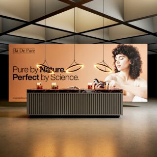 Peach promotional backdrop with a model on the right, a table of beauty products, and the slogan 'Pure by Nature. Perfect by Science.' Neon ring lights hang in front.