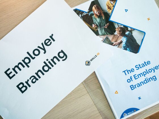 Close-up of marketing brochures on a wooden desk, with bold 'Employer Branding' text and a photo collage on one page and blue/orange design accents nearby.