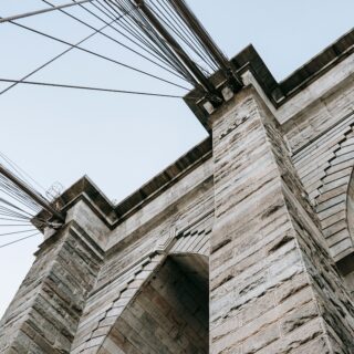 Low-angle view of a stone arch bridge with numerous overhead cables crossing the sky above it.