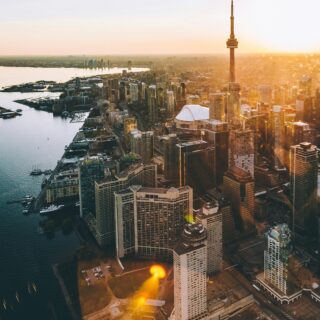 Aerial view of downtown Toronto at sunset with the CN Tower towering over glass-clad skyscrapers along the waterfront.