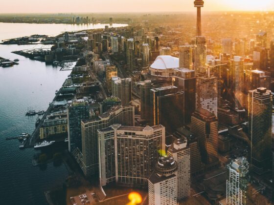 Aerial view of downtown Toronto at sunset with the CN Tower towering over glass-clad skyscrapers along the waterfront.