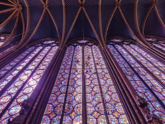 Inside a Gothic cathedral, blue starry vaulted ceiling with ribbed arches and tall colorful stained-glass windows