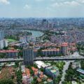 Aerial view of a sprawling city with high-rise towers, dense housing, and winding canals; a large elevated highway runs across the bottom edge.