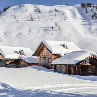 Snowy mountain village with wooden chalets and snow-covered roofs beneath a clear blue sky.