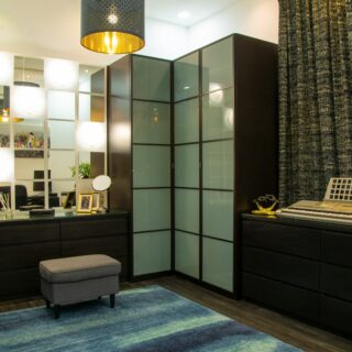 Modern home studio with glass-front cabinets, a keyboard on the right, and a blue rug beneath a gray ottoman.