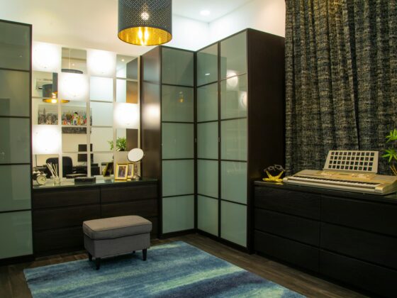 Modern home studio with glass-front cabinets, a keyboard on the right, and a blue rug beneath a gray ottoman.
