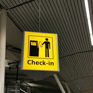 Yellow check-in sign hanging indoors, showing a silhouette of a person at a counter exchanging documents
