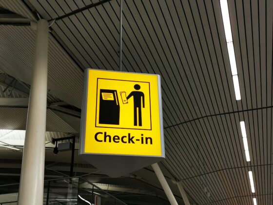 Yellow check-in sign hanging indoors, showing a silhouette of a person at a counter exchanging documents