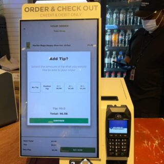 Touchscreen self-service checkout showing order summary and tip options at a counter.