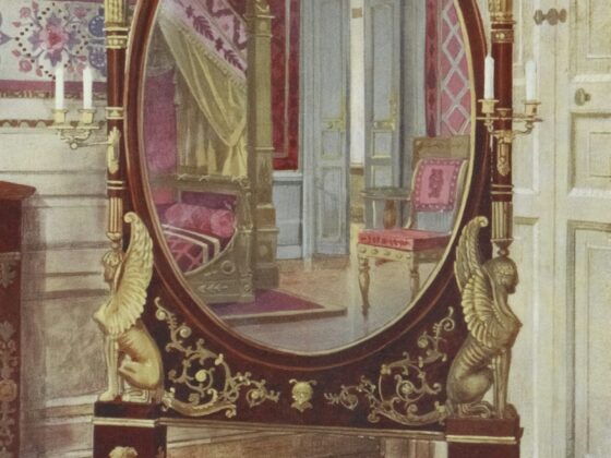 Elegant antique oval mirror on a gilded stand with sculpted figures, reflecting a doorway and pink upholstery in a richly decorated room.