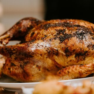 Whole roasted turkey on a white platter with golden, herb-crusted skin and crispy, dark edges.