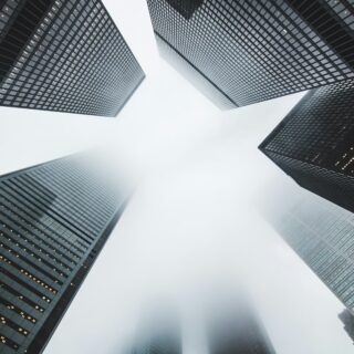 Low-angle view of tall glass skyscrapers converging toward a foggy sky.
