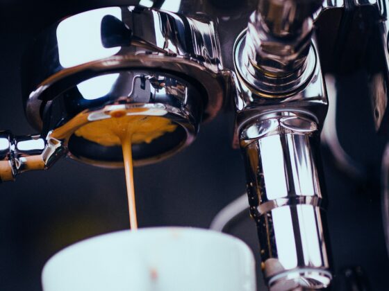 Close-up of chrome motorcycle handlebars with a stream of coffee pouring into a white mug beneath.
