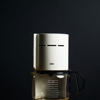 White Braun drip coffee maker with a glass carafe on a wooden table against a dark background, logo visible on the machine.