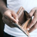 Close-up of hands opening a brown leather wallet with a zipper, revealing empty slots.