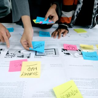 People collaborate around a table, sticking colorful notes on a large planning sheet filled with diagrams and comics.