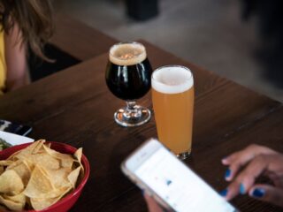 Two beers on a wooden table: a dark stout and a pale ale, with a bowl of tortilla chips nearby.