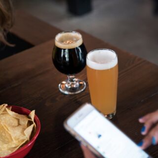 Two beers on a wooden table: a dark stout and a pale ale, with a bowl of tortilla chips nearby.