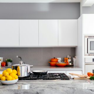 Bright modern kitchen with white flat-panel cabinets, gray walls, and a marble island topped with lemons and flowers.