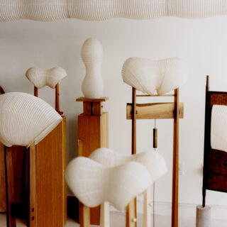 White ribbed wooden sculptures on stands displayed in a bright gallery space.