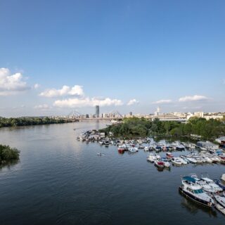 City skyline along a wide river with a busy marina of boats in the foreground under a blue sky.