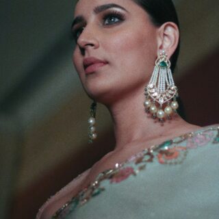 Close-up portrait of a woman wearing elaborate pearl chandelier earrings and makeup.