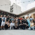 Group of diverse people posing for a photo in a courtyard with string lights and colorful banners above.