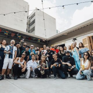 Group of diverse people posing for a photo in a courtyard with string lights and colorful banners above.