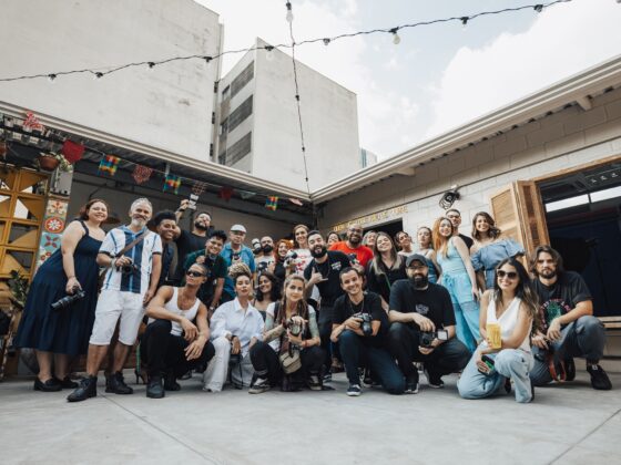 Group of diverse people posing for a photo in a courtyard with string lights and colorful banners above.