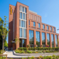 Brick, multi-story building with large glass windows and a landscaped front plaza under a clear blue sky, suggesting a hotel or office complex.