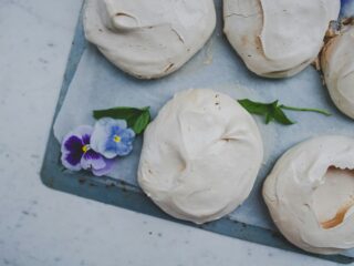 White meringue cookies on a baking sheet with purple pansy flowers for garnish.