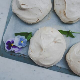White meringue cookies on a baking sheet with purple pansy flowers for garnish.