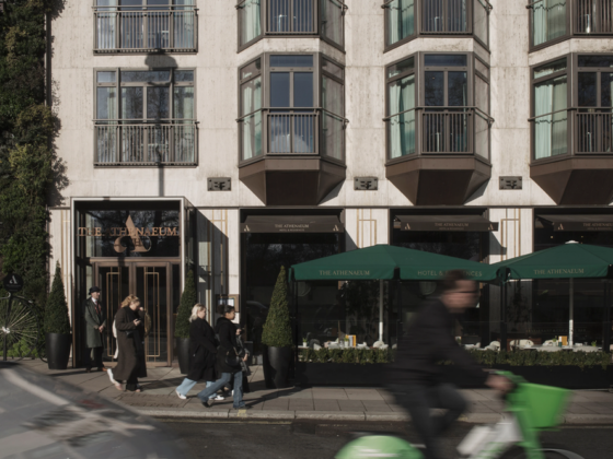 Urban street scene in front of The Athenaeum hotel with pedestrians and a green scooter passing by at street level.