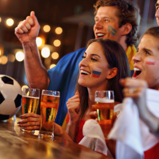 Group of sports fans at a bar cheering for a game, with a soccer ball on the counter and face paint showing team flags.