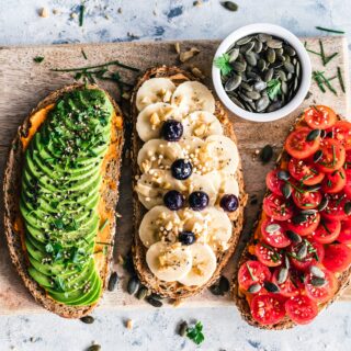 Toast assortment with avocado, banana, and tomato toppings on multigrain bread with seeds on a wooden board