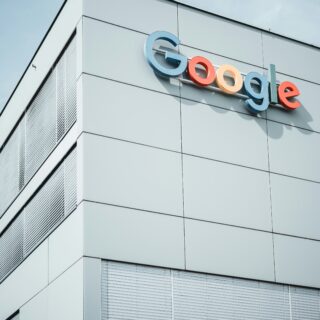 Google logo mounted on the exterior of a modern gray office building against a blue sky.