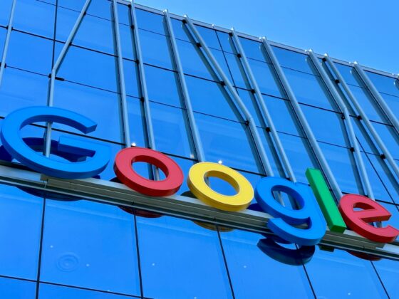 Google logo with blue, red, yellow, green letters on a glass-front modern building there’s a blue sky above.