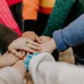 Hands stacked in a circle, showing unity and support among a group of people.
