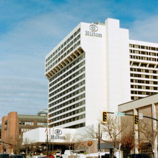 White Hilton hotel building with logo on the corner, urban street in foreground and blue sky above